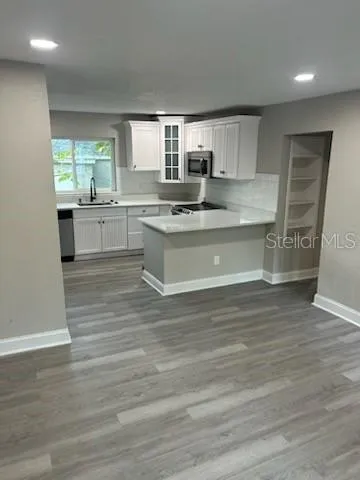 a large kitchen with granite countertop a stove top oven a sink and white cabinets with wooden floor