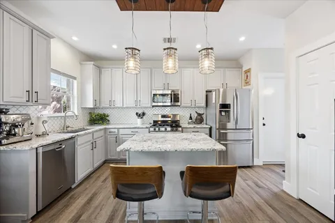 a kitchen with stainless steel appliances kitchen island granite countertop a refrigerator a stove a sink and white cabinets with wooden floor