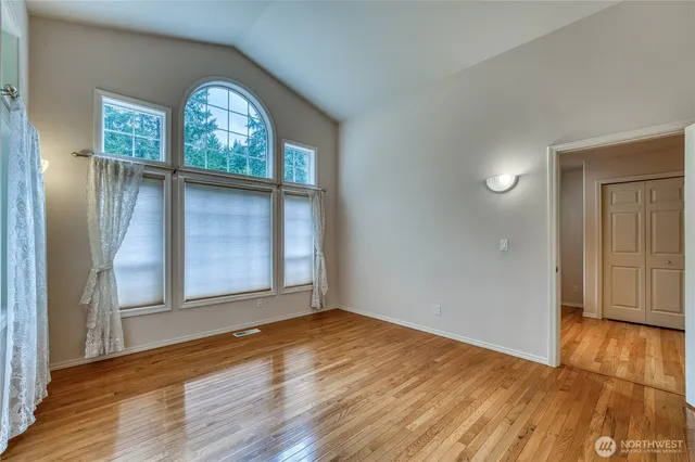 an empty room with wooden floor mirror and windows