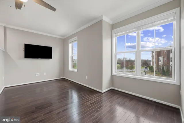 a view of an empty room with wooden floor and a ceiling fan