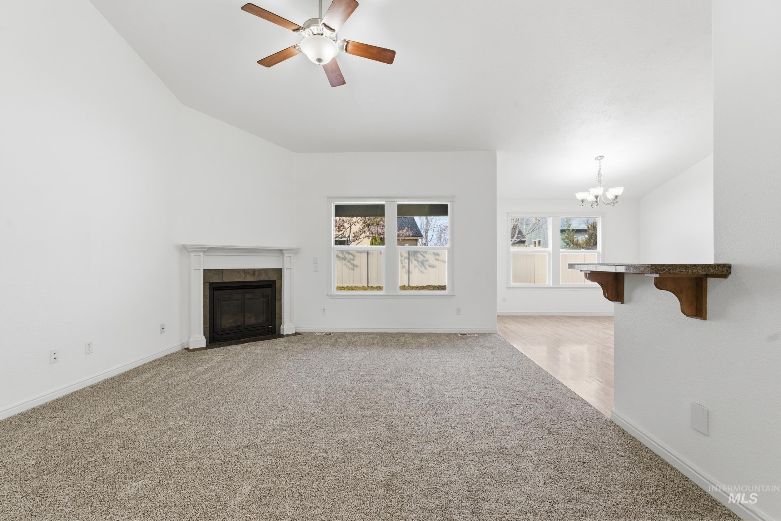 1133 North Powder River Drive Middleton, ID 83644 - Photo 3 of 33 Unfurnished living room featuring light carpet, ceiling fan, a tiled fireplace, and a chandelier