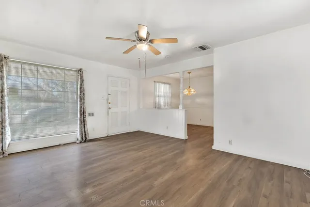 an empty room with wooden floor fan and windows