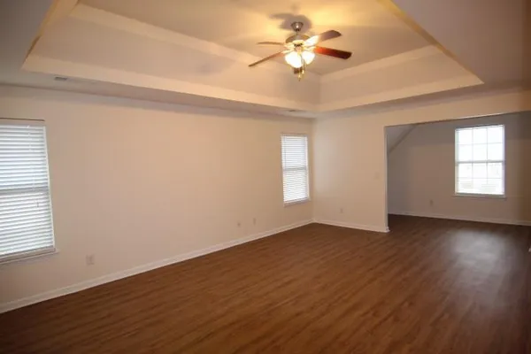 an empty room with wooden floor chandelier fan and windows