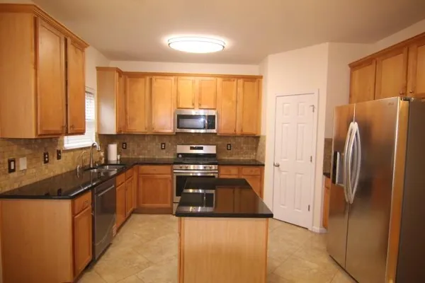 a kitchen with stainless steel appliances granite countertop a refrigerator a stove and a sink with wooden cabinets