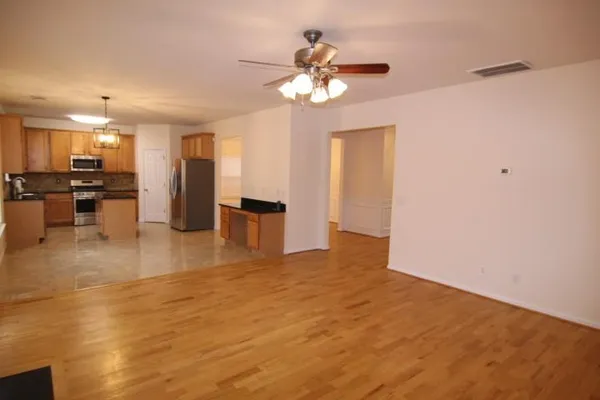 a view of an empty room with a chandelier fan and kitchen view
