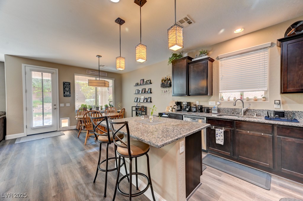 10281 Numaga Road Las Vegas, NV 89178 - Photo 11 of 41 Kitchen with pendant lighting, light stone counters, dark brown cabinets, a kitchen island, and light wood finished floors
