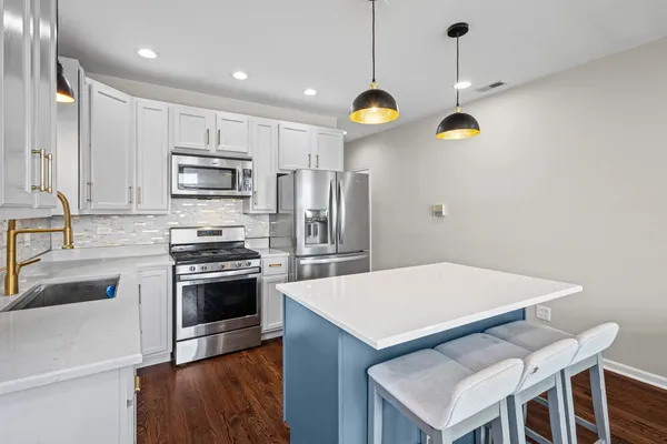 a kitchen with stainless steel appliances granite countertop a sink a stove a refrigerator cabinets and chairs