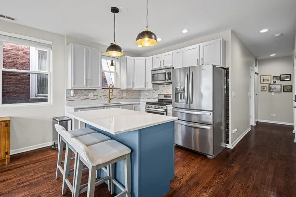 a kitchen with kitchen island a large counter top space stainless steel appliances and windows