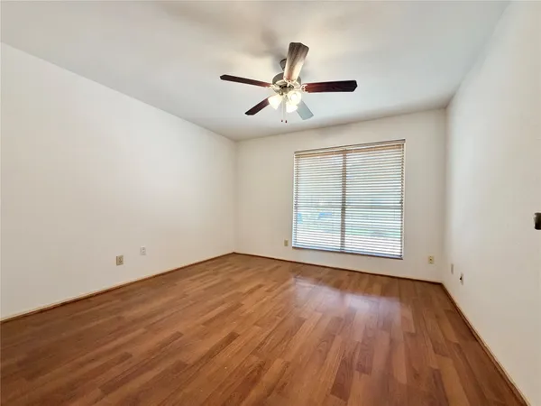 an empty room with wooden floor fan and windows