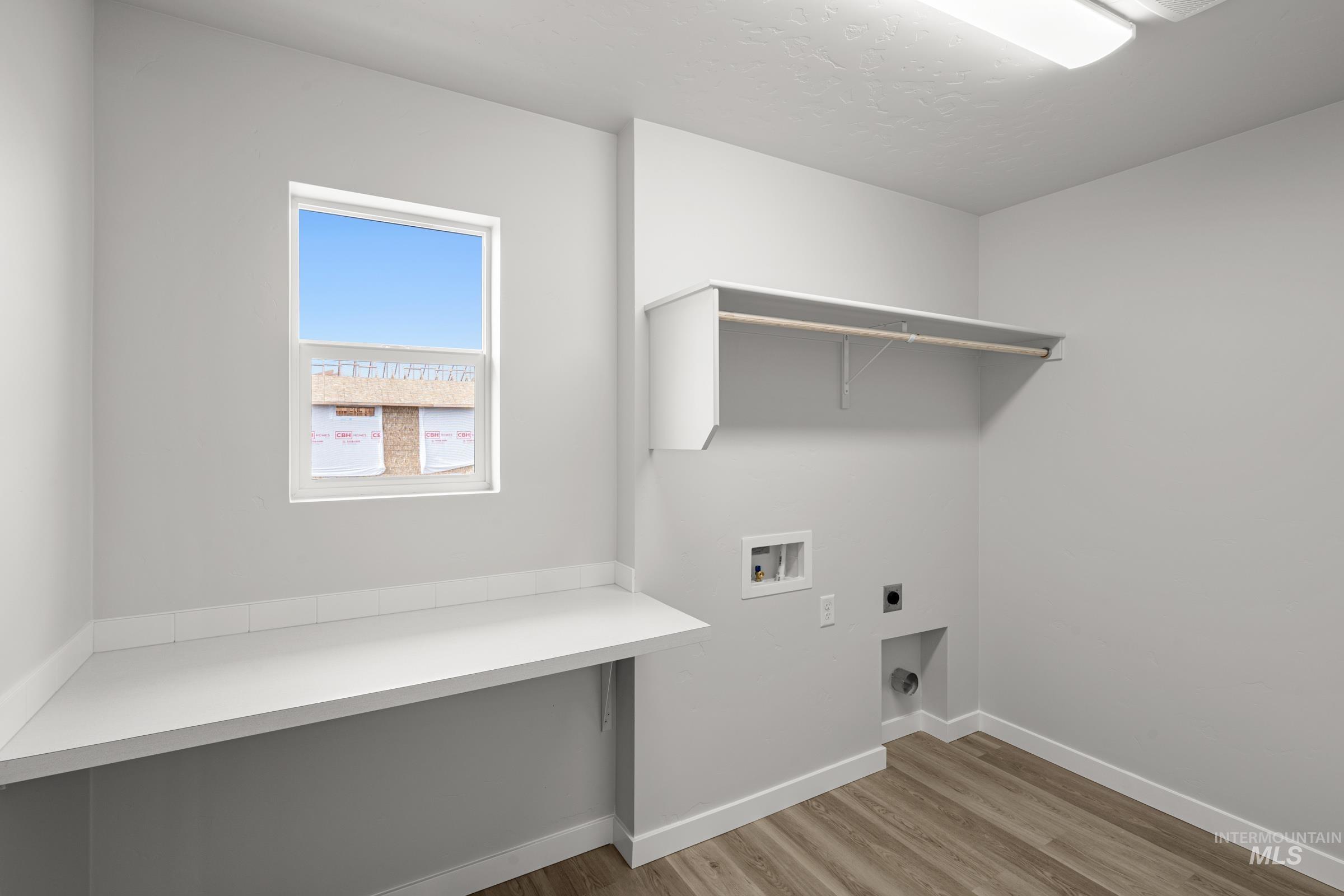 14056 Shiny Spruce Street Caldwell, ID 83607 - Photo 13 of 25 Laundry area featuring wood-finish flooring, a built-in counter with a white surface, a single window, and overhead cabinetry with a clothing rod