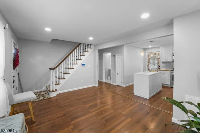a view of an empty room and kitchen with wooden floor