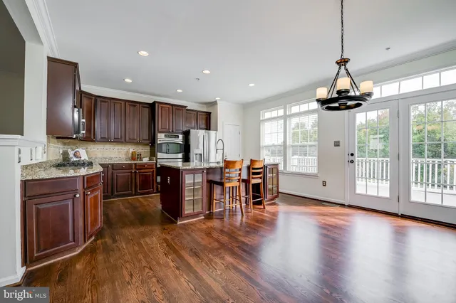 a open kitchen with stainless steel appliances granite countertop a stove top oven a refrigerator a dining table and chairs with wooden floor