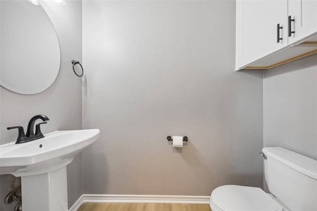 753 Summerfield Drive Allen, TX 75002 - Photo 18 of 40 Pedestal sink with a matte black faucet, wall-mounted circular mirror, and overhead white cabinetry with black hardware
