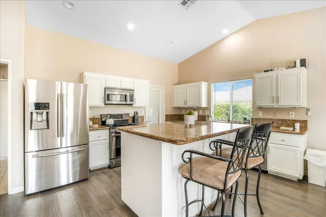 a kitchen with stainless steel appliances granite countertop a refrigerator a stove a sink dishwasher and white cabinets with wooden floor