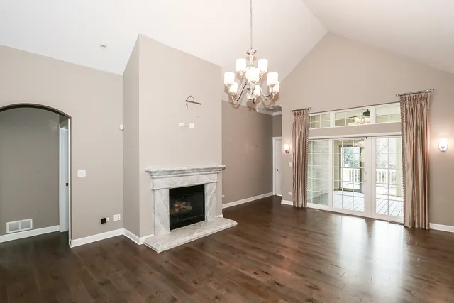 an empty room with wooden floor fireplace and chandelier
