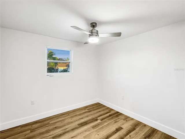 an empty room with wooden floor ceiling fan and windows