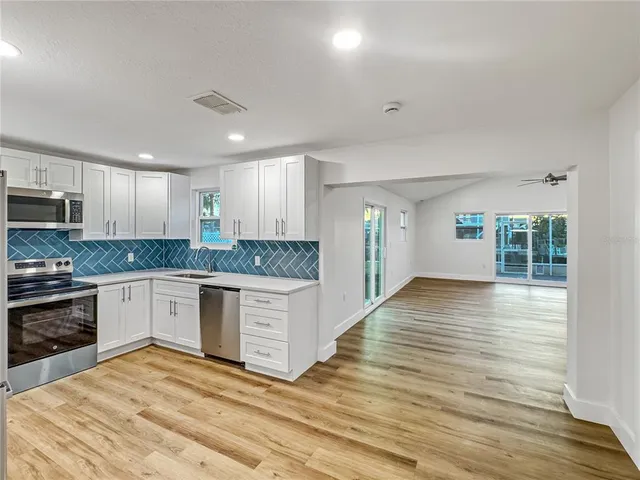 a kitchen with granite countertop a stove top oven a sink dishwasher a refrigerator and white cabinets with wooden floor