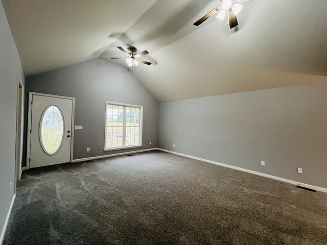 an empty room with a chandelier fan and windows
