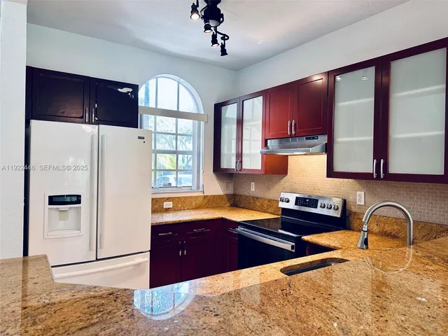 a kitchen with stainless steel appliances granite countertop a refrigerator a sink dishwasher a stove and white countertops with wooden floor