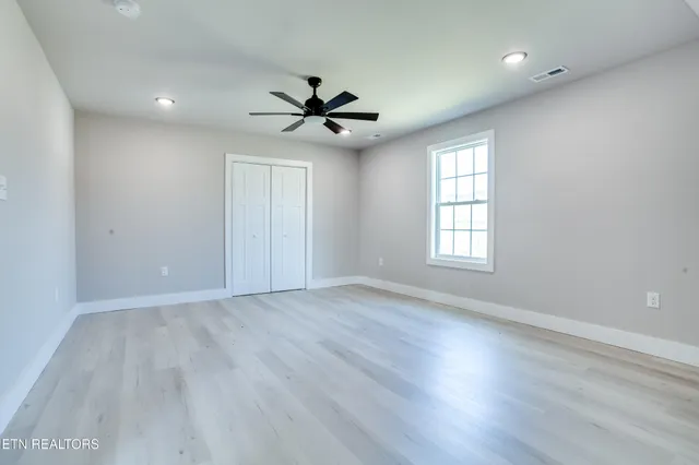 an empty room with wooden floor fan and windows
