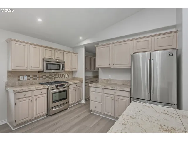 a kitchen with stainless steel appliances granite countertop a stove a sink and a refrigerator with white cabinets
