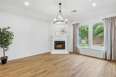 a view of an empty room with wooden floor fireplace and a window