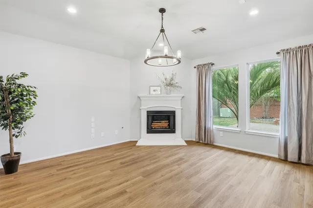 a view of an empty room with wooden floor fireplace and a window