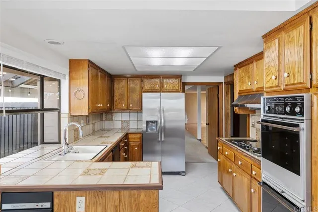 a kitchen with stainless steel appliances granite countertop a refrigerator a stove and a sink with wooden cabinets