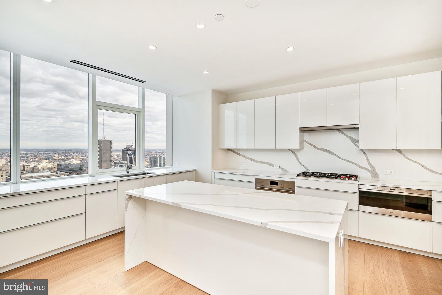 301 South Broad Street, Unit 4001 Philadelphia, PA 19107 - Photo 20 of 84 a kitchen with a stove a sink and white cabinets with wooden floor next to windows