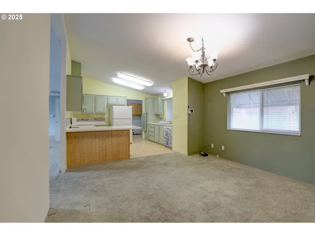 a view of an empty room with kitchen and window