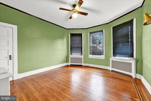 an empty room with wooden floor a ceiling fan and windows