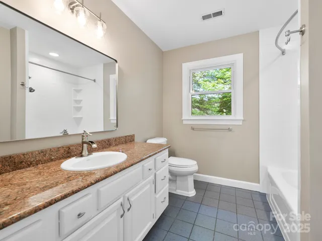a bathroom with a granite countertop sink a large mirror a toilet and a window