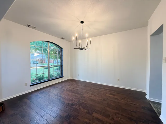 an empty room with wooden floor chandelier and windows