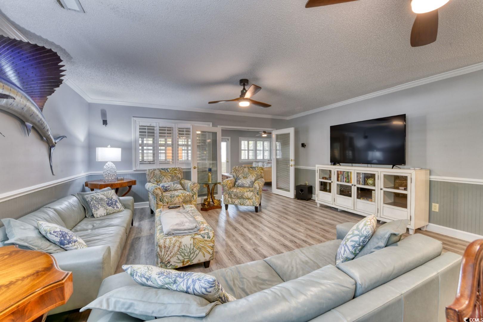 3714 Jordan Landing Road Murrells Inlet, SC 29576 - Photo 16 of 39 Living room with wainscoting, a textured ceiling, wood finished floors, crown molding, and a ceiling fan
