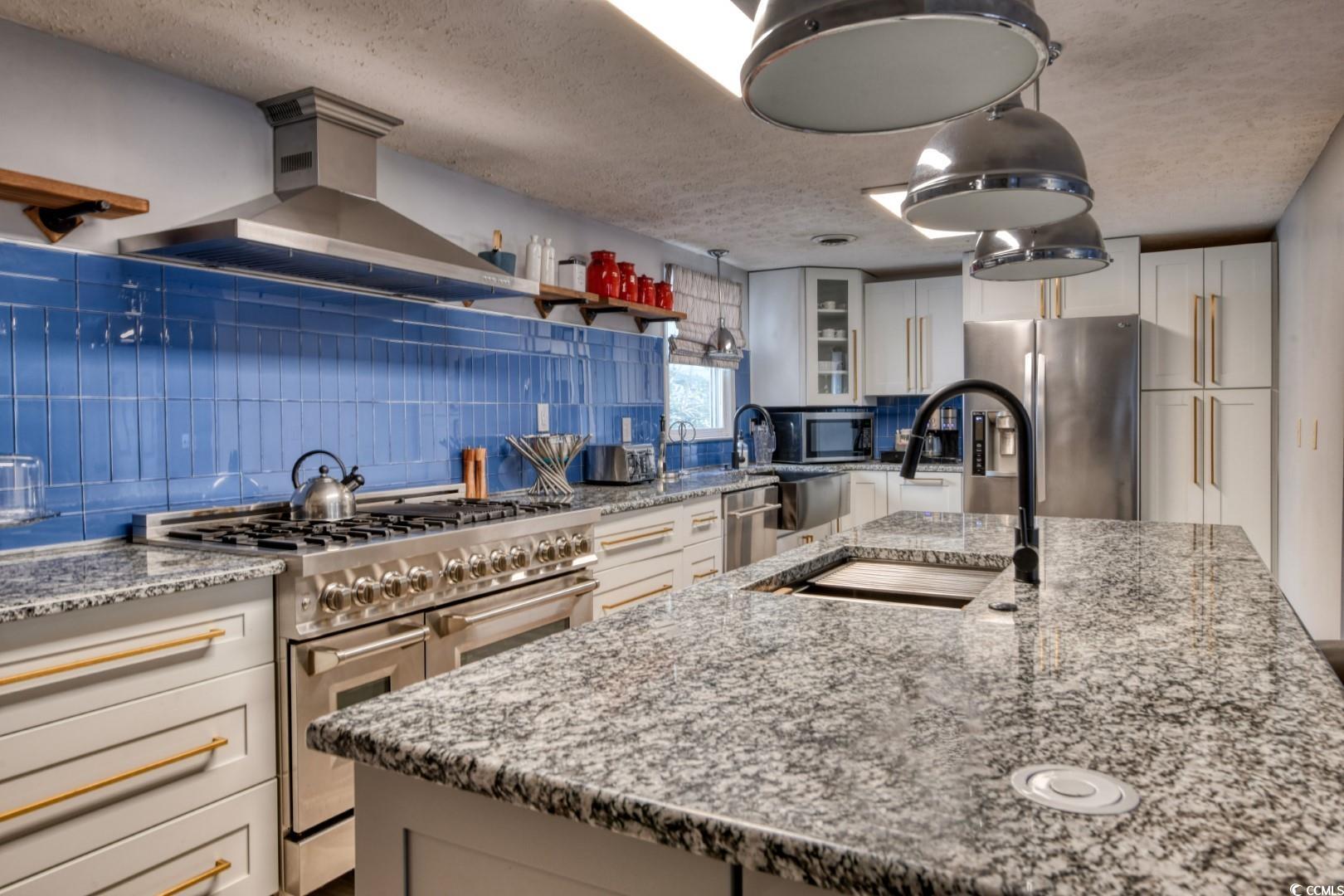 3714 Jordan Landing Road Murrells Inlet, SC 29576 - Photo 5 of 39 Kitchen with appliances with stainless steel finishes, light stone countertops, wall chimney range hood, glass insert cabinets, and a textured ceiling
