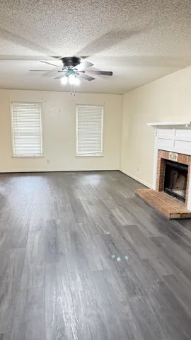 an empty room with wooden floor fireplace and chandelier fans