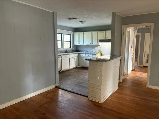 a kitchen with stainless steel appliances granite countertop a white cabinets a sink a stove and a wooden floor