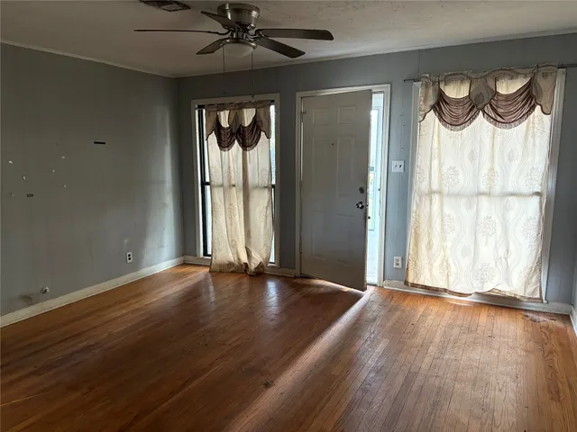 an empty room with wooden floor fan and windows