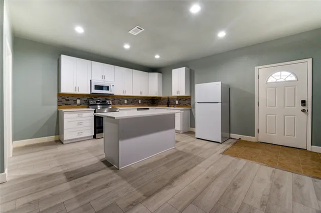 an empty room with wooden floor ceiling fan and kitchen view