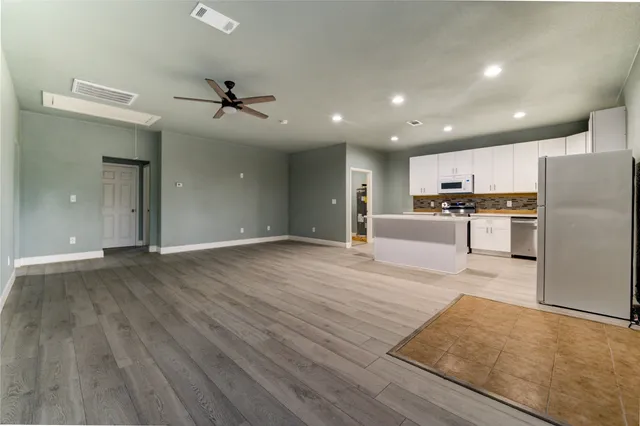 a large kitchen with kitchen island a stove a sink dishwasher a refrigerator and white cabinets with wooden floor