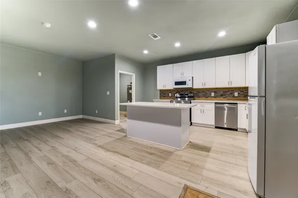 a large kitchen with kitchen island a stove a sink dishwasher a refrigerator and white cabinets with wooden floor