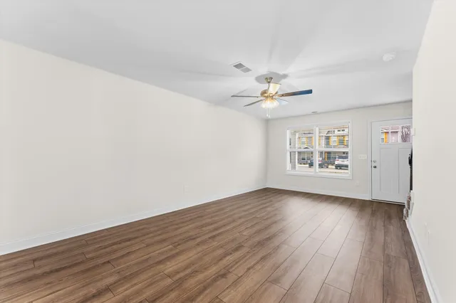 an empty room with wooden floor chandelier fan and windows