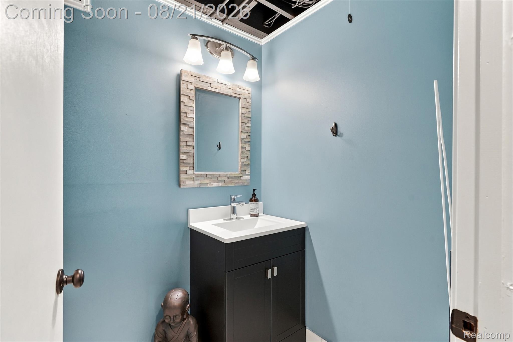 6060 Ford Road Commerce Township, MI 48382 - Photo 34 of 58 Vanity with integrated sink, rectangular mirror with a stone-finish frame, and a three-light fixture
