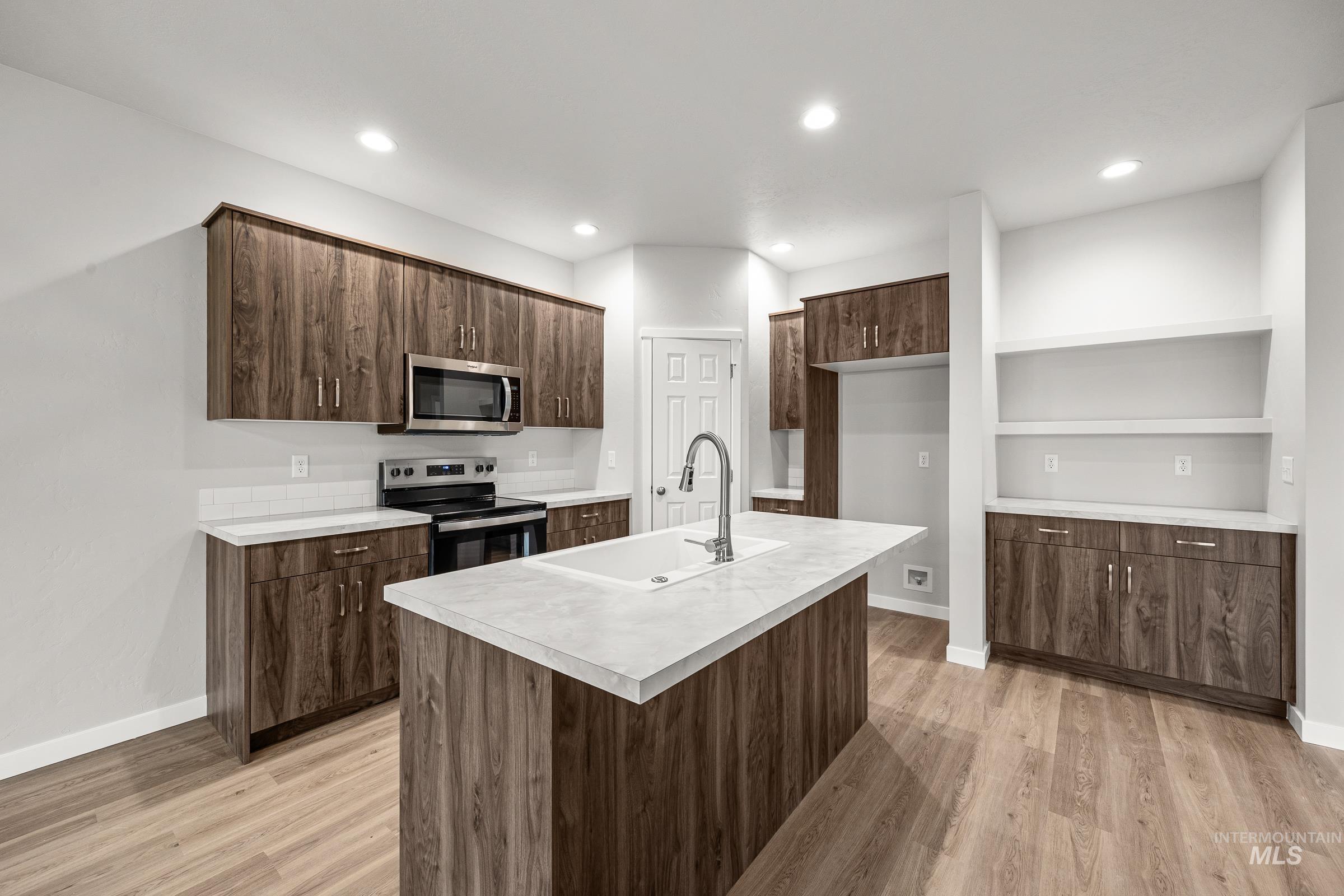 13656 Redway Court Caldwell, ID 83607 - Photo 4 of 21 Kitchen featuring a central island with an undermount sink, wood-finish cabinetry, stainless steel appliances, light-toned countertops, and wood-finish flooring