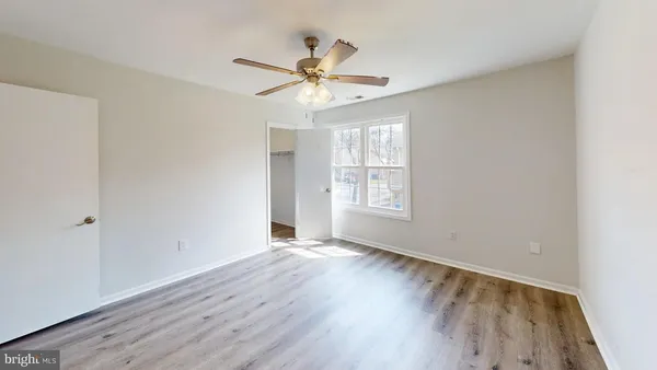 an empty room with wooden floor chandelier fan and windows