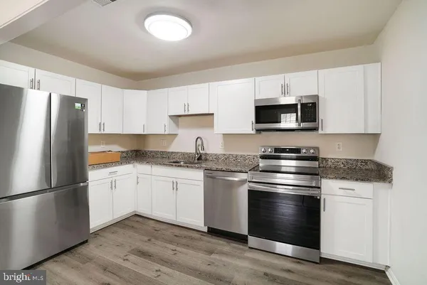a kitchen with granite countertop a refrigerator stove and white cabinets