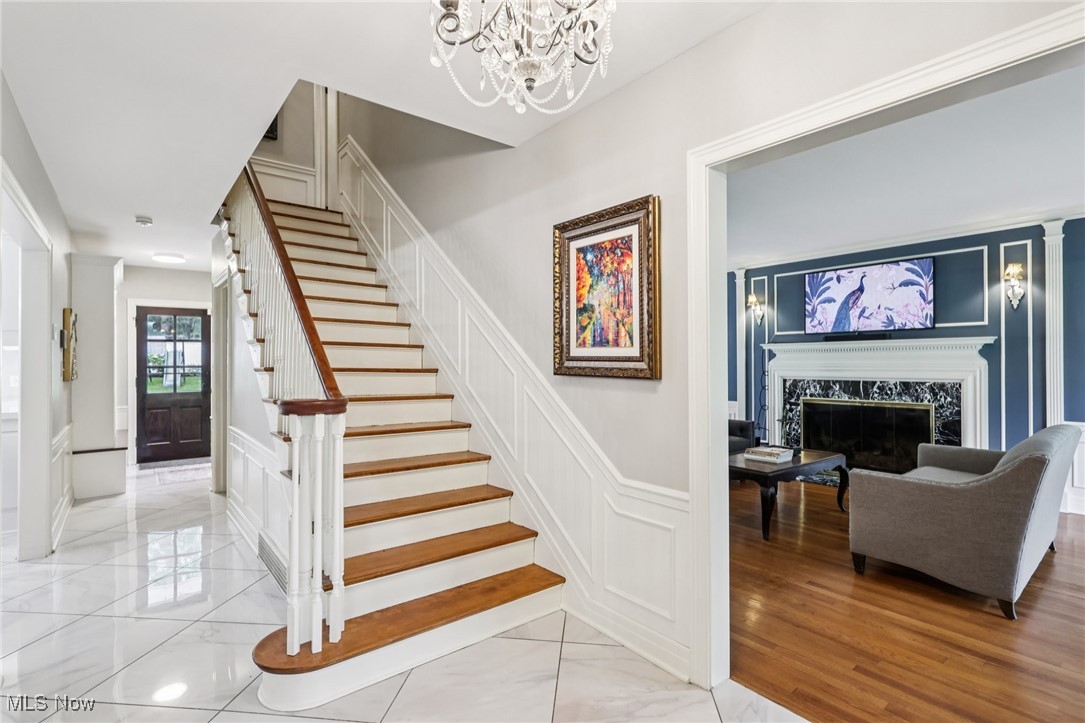 75 North Wheaton Road Akron, OH 44313 - Photo 3 of 40 Stairs with a decorative wall, a chandelier, marble finish flooring, a fireplace, and wainscoting