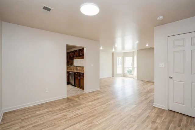 a view of a kitchen and an empty room with wooden floor