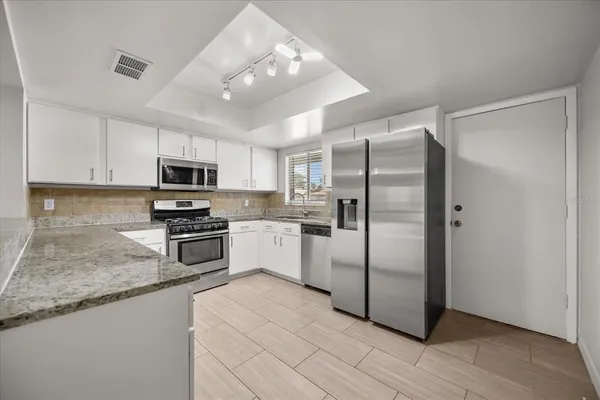 a kitchen with granite countertop a refrigerator a sink a stove a microwave and cabinets