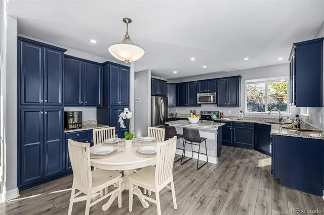 a kitchen with stainless steel appliances kitchen island granite countertop wooden floors cabinets a dining table and chairs